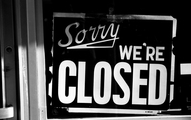 Black and white image of sign in store window that reads, "Sorry, we're closed."